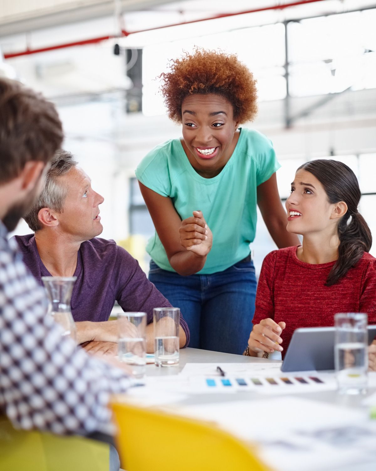 Trois personnes en réunion autour d'une table, l'une debout explique un point aux deux autres.